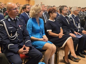 W rzędach na sali ludzie siedzą zwróceni w kierunku sceny.