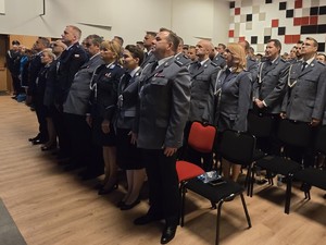 Na dużej sali umundurowani policjanci wstali z krzeseł i stoją na baczność