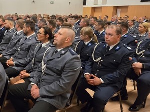 Ludzie siedzący na krzesłach na dużej sali, zwróceni w kierunku sceny.
