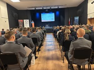 Na dużej sali siedzą ludzie zwróceni w kierunku sceny.