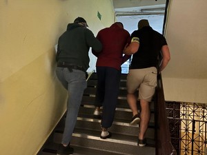 Dwóch nieumundurowanych policjantów prowadzi po schodach zatrzymanego