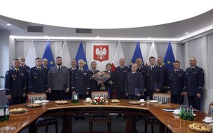 Wspólne zdjęcie grupowe laureatów i uczestników uroczystości. Policjanci umundurowani stoją za stołem. W tle godło Polski.