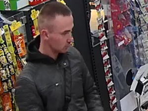 Mężczyzna młody w kurtce ze skóry w sklepie pomiędzy półkami.