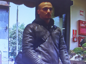 Na zdjęciu młody mężczyzna w kurtce ze skóry wchodzi do sklepu.