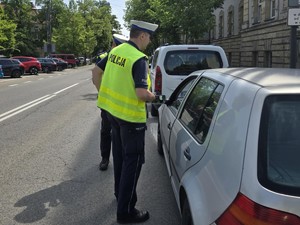 Dwóch policjantów umundurowanych w kamizelkach odblaskowych prowadzi kontrolę pojazdu