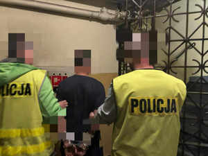 Dwóch policjantów w kamizelkach odblaskowych wyprowadza zatrzymanego z PDOZ.