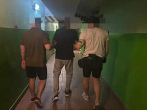 Mężczyzna zatrzymany prowadzony korytarzem przez dwóch nieumundurowanych policjantów.