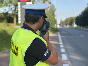 Na zdjęciu policjant stojący przy drodze dokonuje pomiaru prędkości.