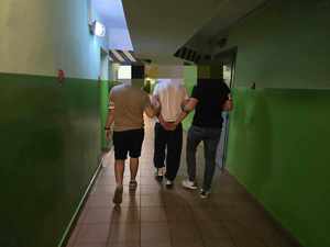 Dwóch nieumundurowanych policjantów prowadzi zatrzymanego korytarzem.