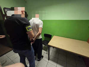 Nieumundurowany policjant zakłada zatrzymanemu kajdanki.