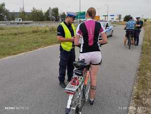 Na zdjęciu widzimy radiowóz oraz dwóch policjantów ruchu drogowego którzy prowadzą kontrolę kierujących rowerami.