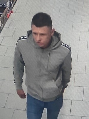 Młody mężczyzna w jasnej szarej bluzie i krótkich ciemnych włosach