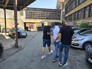 Na zdjęciu dwóch nieumundurowanych policjantów prowadzi mężczyznę do samochodu.
