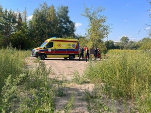 Ratownicy oraz policjanci wkładają do karetki osobą poszkodowaną na noszach.