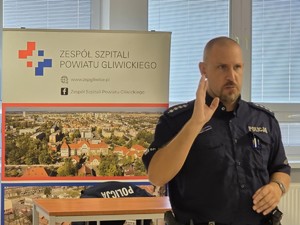 Asp. szt. Jarosław Stachel prowadzi wykład. W tle baner szpitala pyskowickiego.