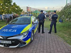 Radiowóz oznakowany i dwóch policjantów stojących przy radiowozie.