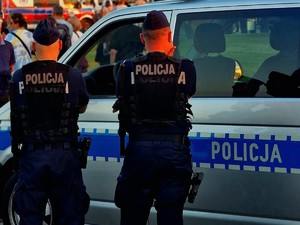 Policjanci stojący przy radiowozie. W tle uczestnicy koncertu.