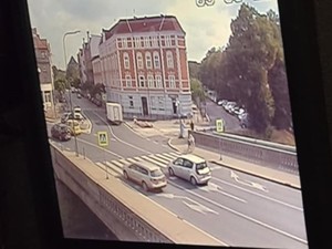 Widok ulicy - w rejonie przejścia dla pieszych jadą dwa samochody osobowe.