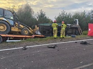 Na zdjęciu zobaczymy pracujących strażaków przy tirze, który jest oparty na boku  w rowie w rejonie skrzyżowania