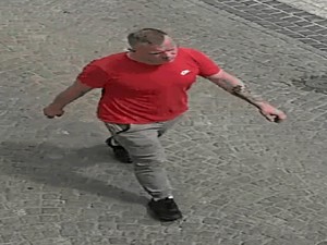 Zdjęcie z kamery. Młody mężczyzna w czerwonej koszulce i szarych spodniach idzie machając rękami.