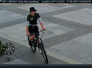 chłopak jadący na rowerze, który dokonał jego kradzieży, ubrany w ciemne ubrania i czarną czapkę.