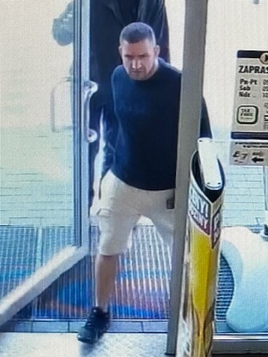 sprawca kradzieży wchodzący do sklepu, ubrany w bluzkę z długim rękawem koloru ciemnego oraz jasnych krótkich spodenkach