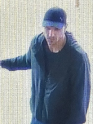 sprawca kradzieży wchodzący do sklepu, ubrany w bluzę z długim rękawem i czapkę koloru ciemnego