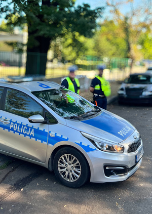 Dwóch policjantów umundurowanych stojących przy radiowozie oznakowanym.
