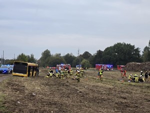 Widok z oddali autobusu stojącego w polu i trwającej akcji ratunkowej.