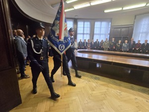 Poczet sztandarowy. W tle stoją umundurowani funkcjonariusze Policji.