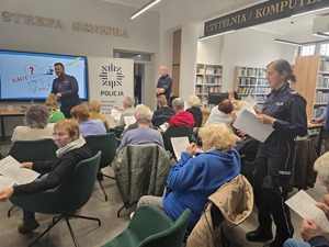 Policjantka rozdaje uczestnikom debaty ankiety ewaluacyjne.