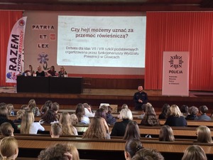 Na auli podczas debaty siedzą uczniowie szkół gliwickich. Na scenie siedzą zaproszeni goście. W tle wyświetla się prezentacja.