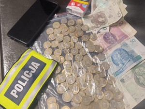 Na zdjęciu zatrzymany telefon, opaska z napisem POLICJA oraz pieniądze w bilonie oraz banknoty.