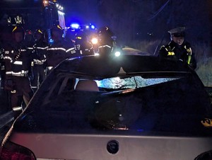 Z bliska widać jasny pojazd biorący udział w wypadku. Dalej w ciemności świecą elementy odblaskowe znajdujące się na umundurowaniu strażaków.