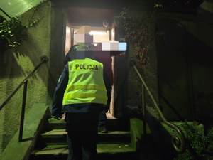 Dwóch policjantów wprowadza zatrzymanego do budynku po schodach.