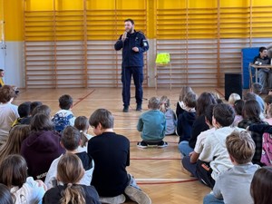 Policjant przemawia do uczniów siedzących na sali gimnastycznej.