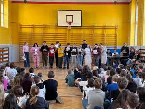 Na sali  gimnastycznej część uczniów siedzi, a część występuje.