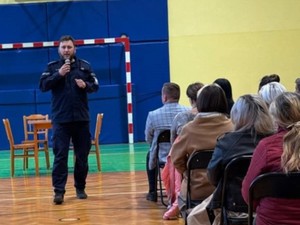 Z mikrofonem przez rodzicami uczniów szkoły w Wilcze przemawia asp. Mateusz Piórkowski.