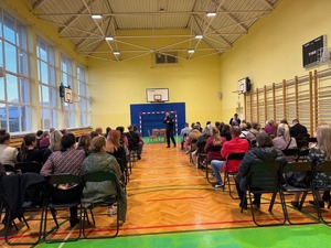 Z mikrofonem, na sali gimnastycznej, przed rodzicami uczniów szkoły w Wilczej przemawia asp. Mateusz Piórkowski.