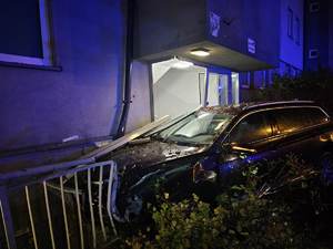 Rozbity samochód stoi przy oświetlonej klatce schodowej.