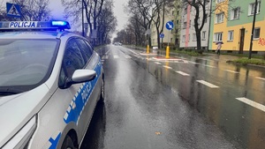 Widok na pustą ulicę, w oddali stojący w poprzek radiowóz oznakowany.