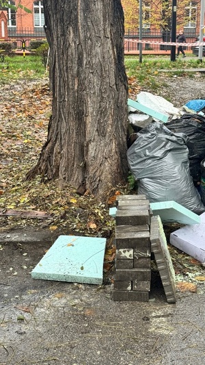 Granat z okresu II Wojny Światowej leżący pod drzewem. A dookoła leżące śmieci, stare materiały budowlane