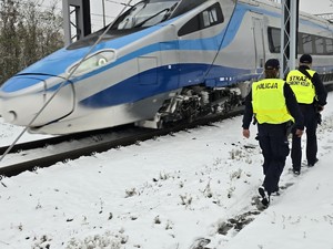 Patrol składający się z policjanta i funkcjonariusz Straży Ochrony Kolei sprawdzają rejon torowiska. Obok przejeżdża pendolino.
