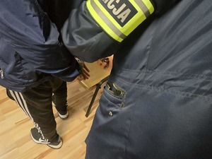 policjant nieumundutowany w pomieszczeniu zakłada zatrzymanemu kajdanki.