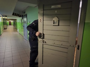 Pomieszczenie dla osób zatrzymanych. Policjant otwiera drzwi