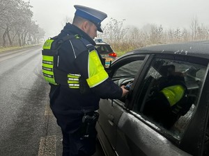 Policjant umundurowany stoi przy samochodzie badając trzeźwość kierującego.