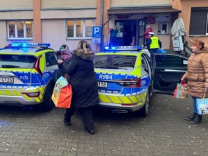 Pracownicy Oddziału Pomocy Społecznej noszą paczki z radiowozu do budynku.