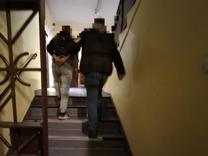 Nieumundurowany policjant prowadzi zatrzymanego w kajdankach p[o schodach