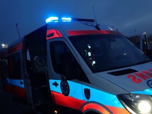 Karetka pogotowia ratunkowego stojąca na jesni z włączonymi niebieskimi światłami.
