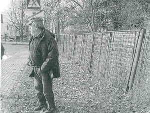 Na zdjęciu starszy mężczyzna stojący przy ogrodzeniu.